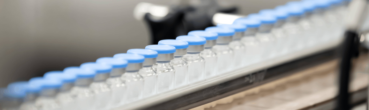 Close-up of a pharmaceutical production line showing glass vials being processed in a cleanroom environment.